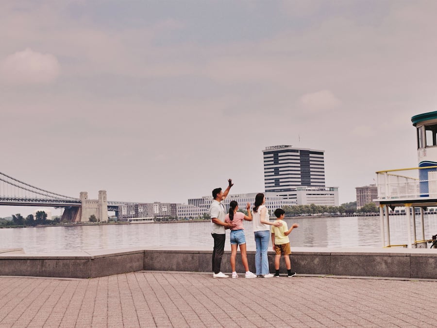 A waterfront promenade with a bridge in the background, a boat dock, and a building with a sign.