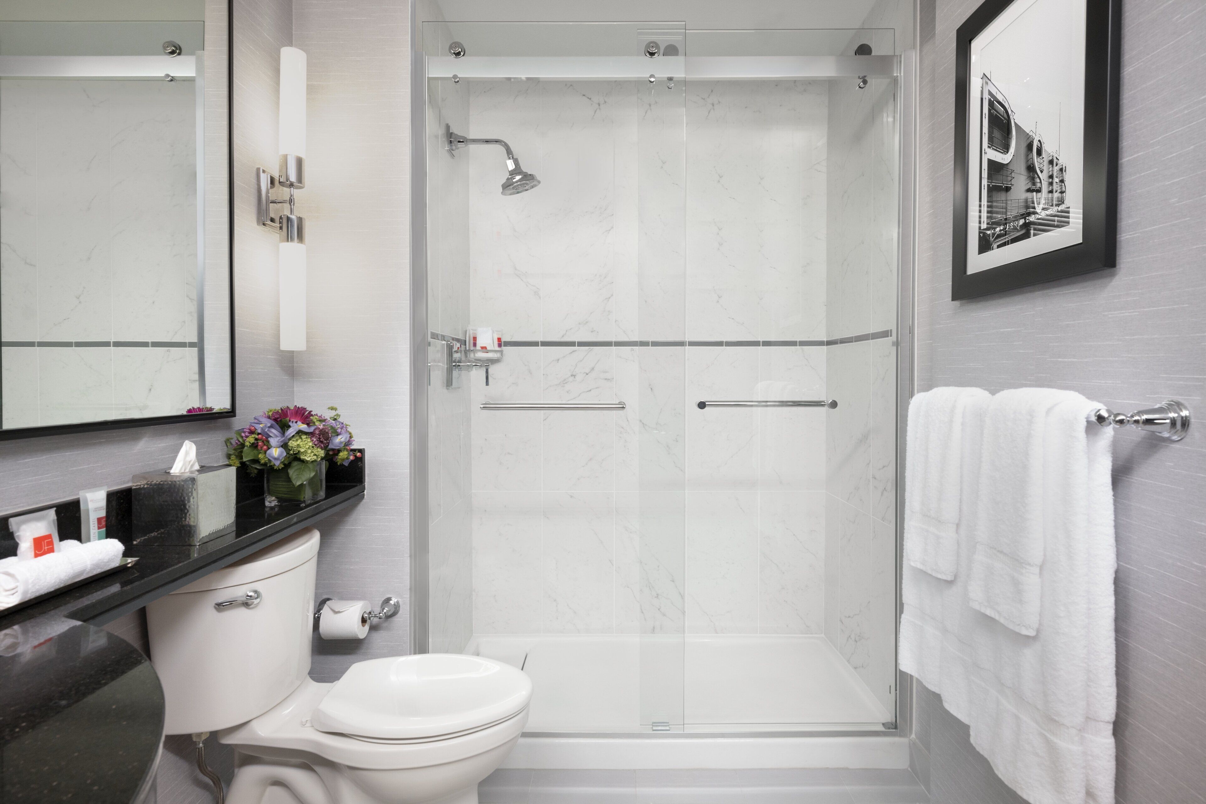 A modern bathroom with a glass-enclosed shower, a toilet, and a sink with toiletries.