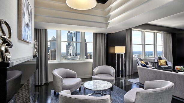 A modern hotel room with a city view, a sofa set, a round table, and a large window.