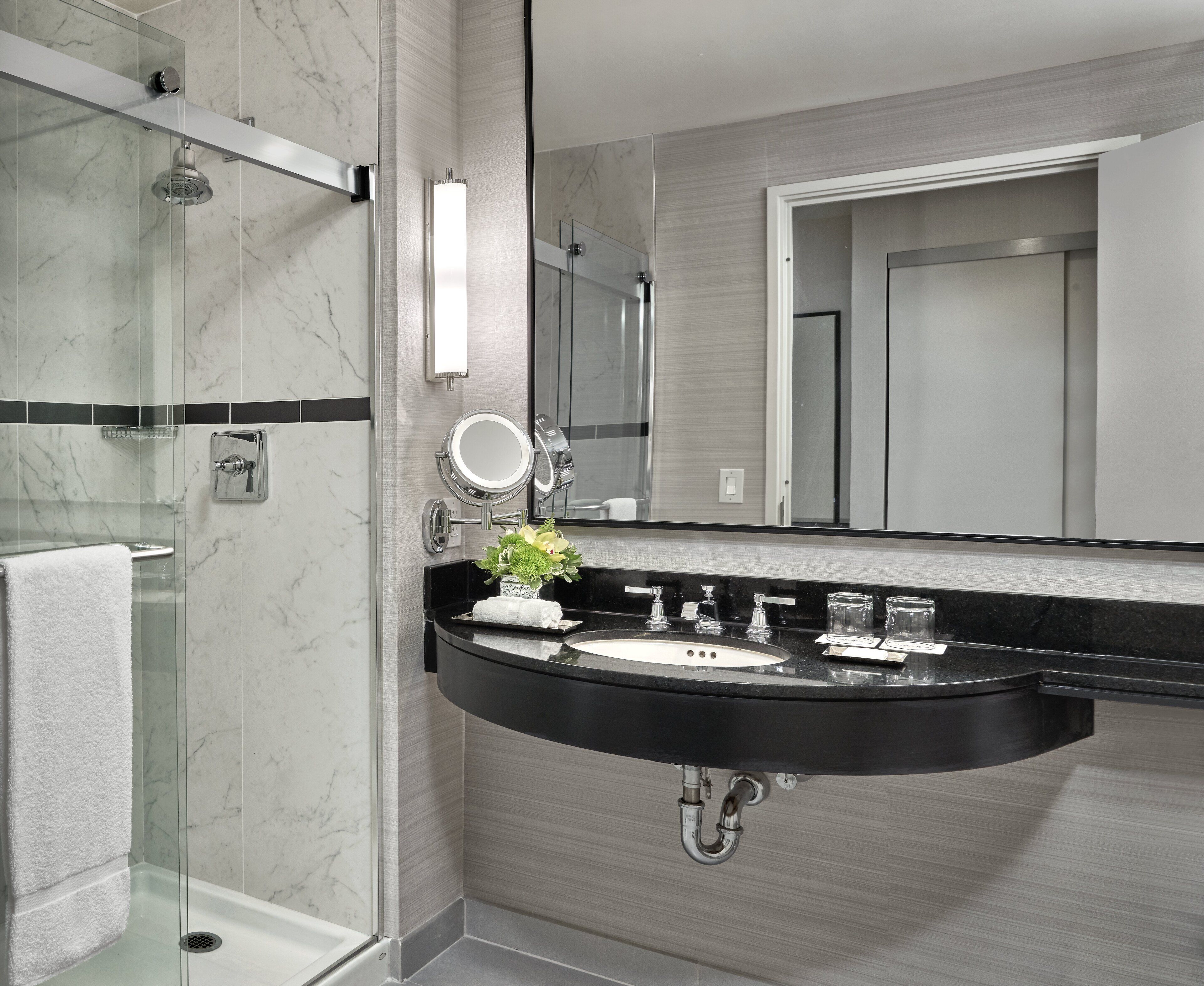 A modern bathroom with a glass-enclosed shower, a black sink with a marble countertop, and a large mirror above the sink.