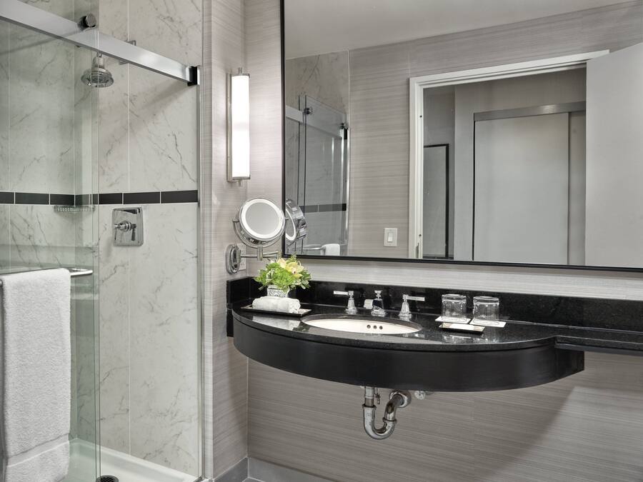 Ein modernes Badezimmer mit einer gläsernen Duschkabine, einem schwarzen Waschbecken mit Marmorplatte und einem großen Spiegel darüber.