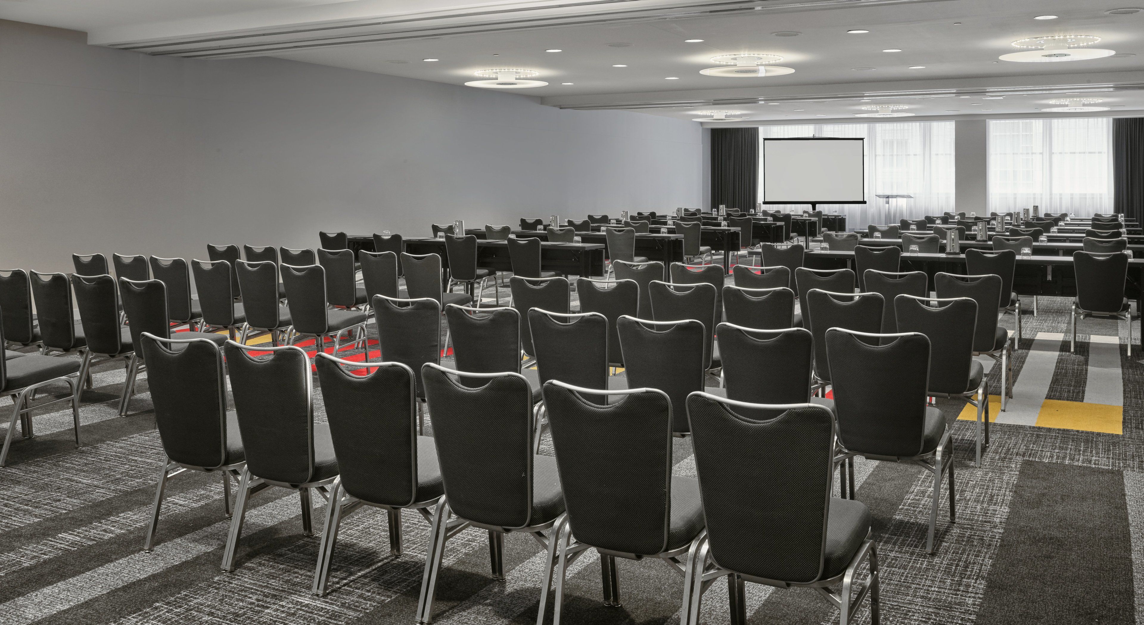 Un salón de conferencias con hileras de sillas, una pantalla grande y suelo alfombrado.