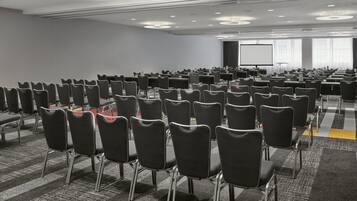Un salón de conferencias con hileras de sillas, una pantalla grande y suelo alfombrado.