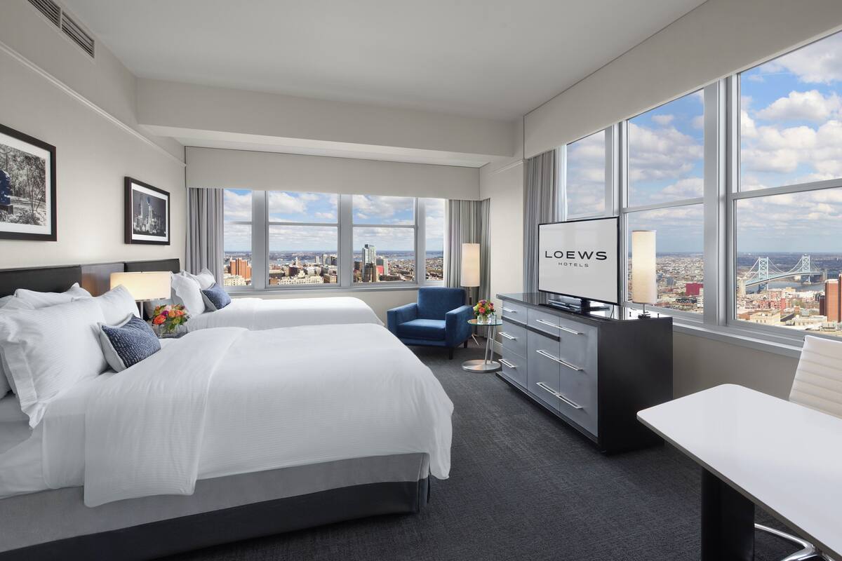 A hotel room with a large bed, a desk, a TV, and a view of the city.