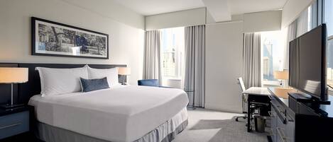 A hotel room with a large bed, a desk, a chair, a TV, and a window with curtains.