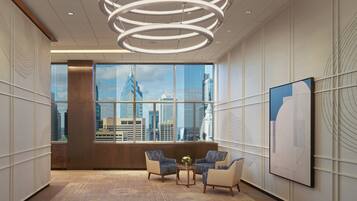 En modern hotellobby med ett stort fönster som ger utsikt över staden, två fåtöljer, ett bord med en vas och en unik taklampa.