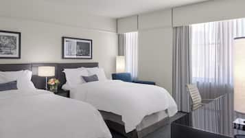 Quarto de hotel com duas camas, uma mesa, uma cadeira e varanda com cortinas.
