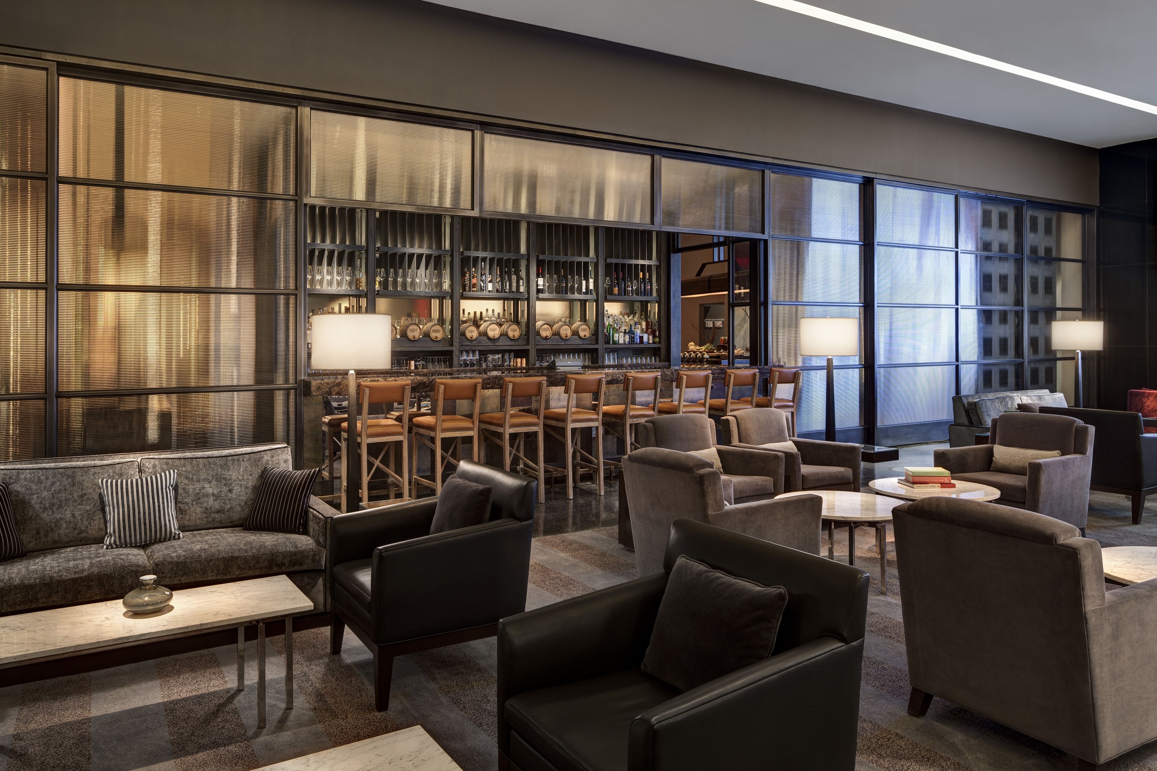 Een moderne lounge met leren banken, fauteuils en een bar met flessen op de planken.
