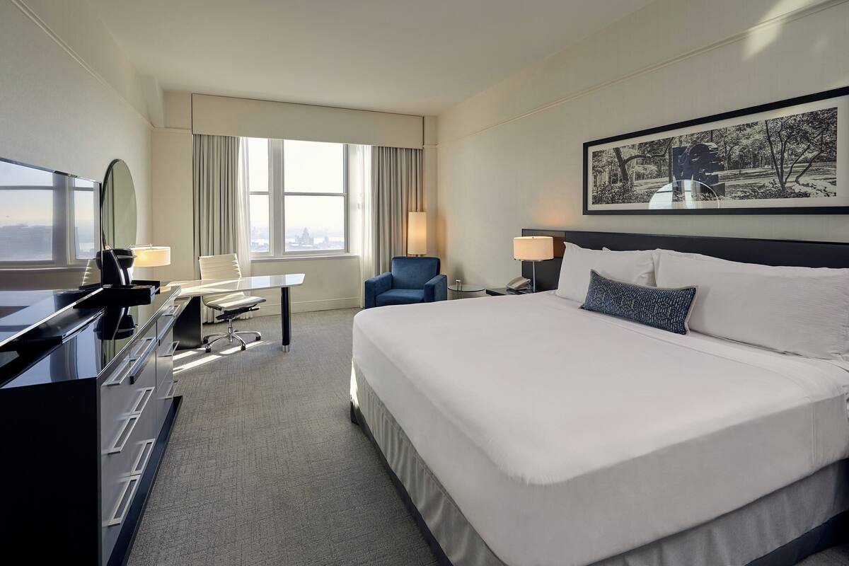 A hotel room with a large bed, a desk with a chair, a TV, and a window with curtains.