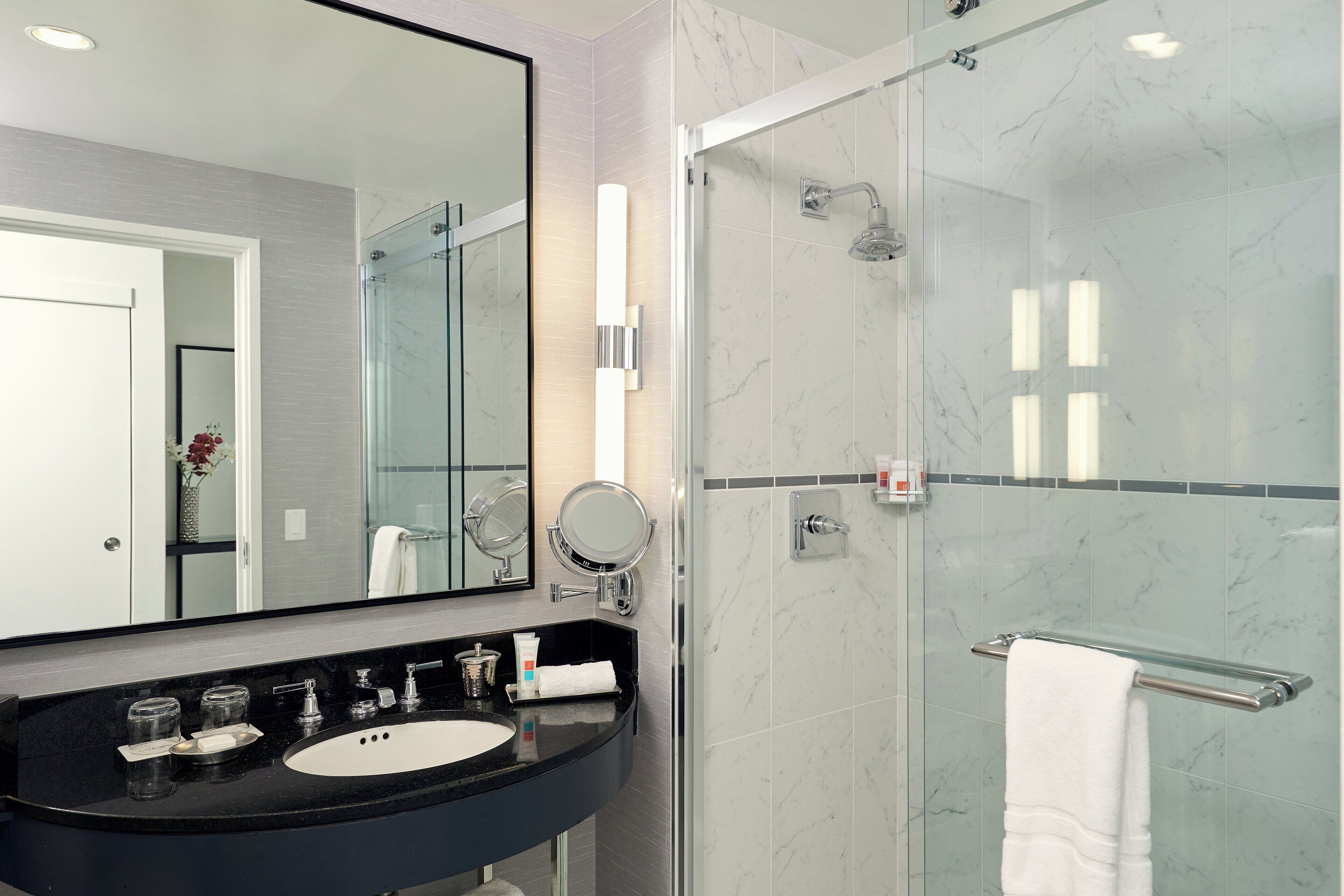A modern bathroom with a black sink, a large mirror, a glass-enclosed shower, and a white towel on a towel rack.