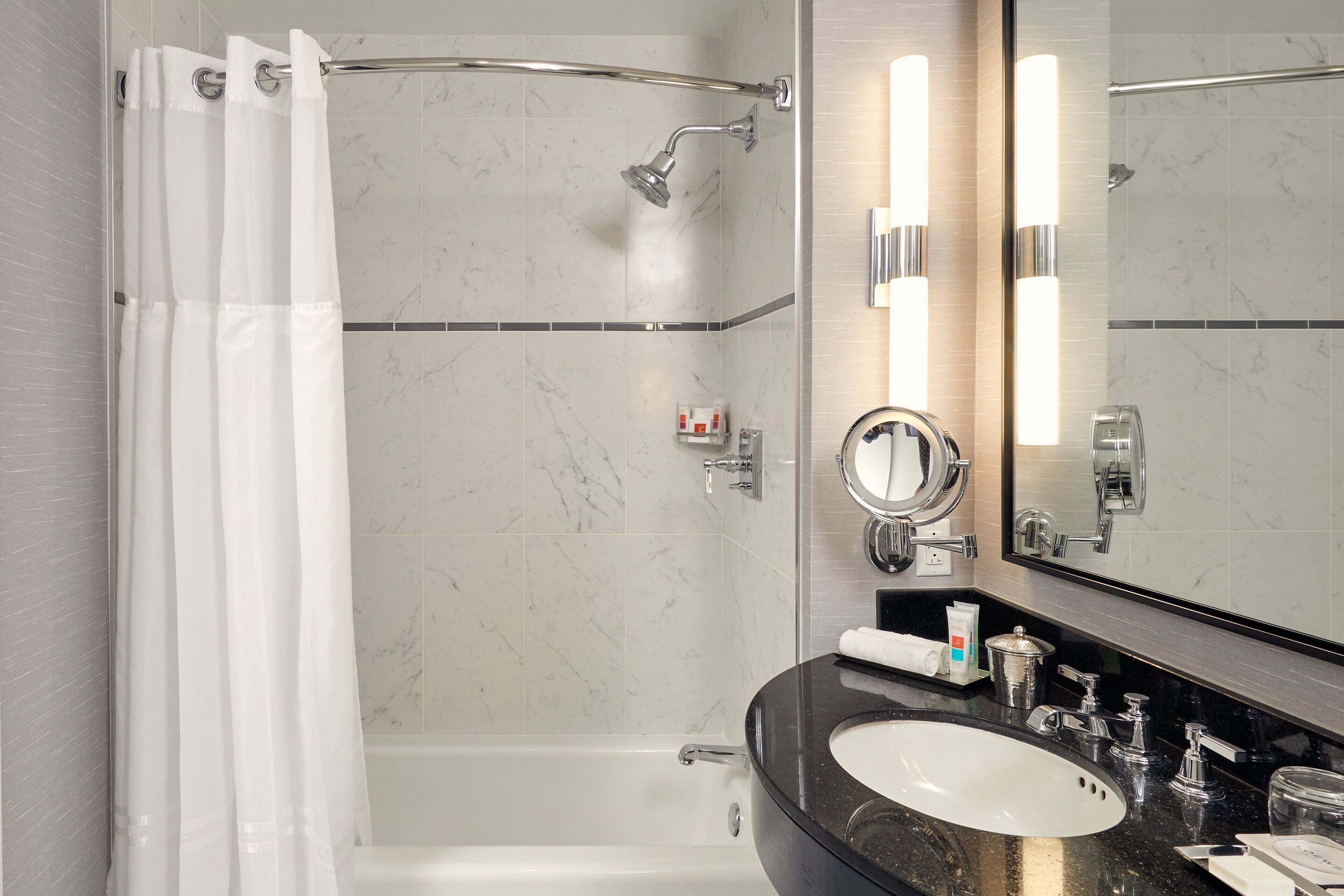 Un baño moderno con bañera, ducha con puerta de cristal, tocador con lavabo y un espejo grande.