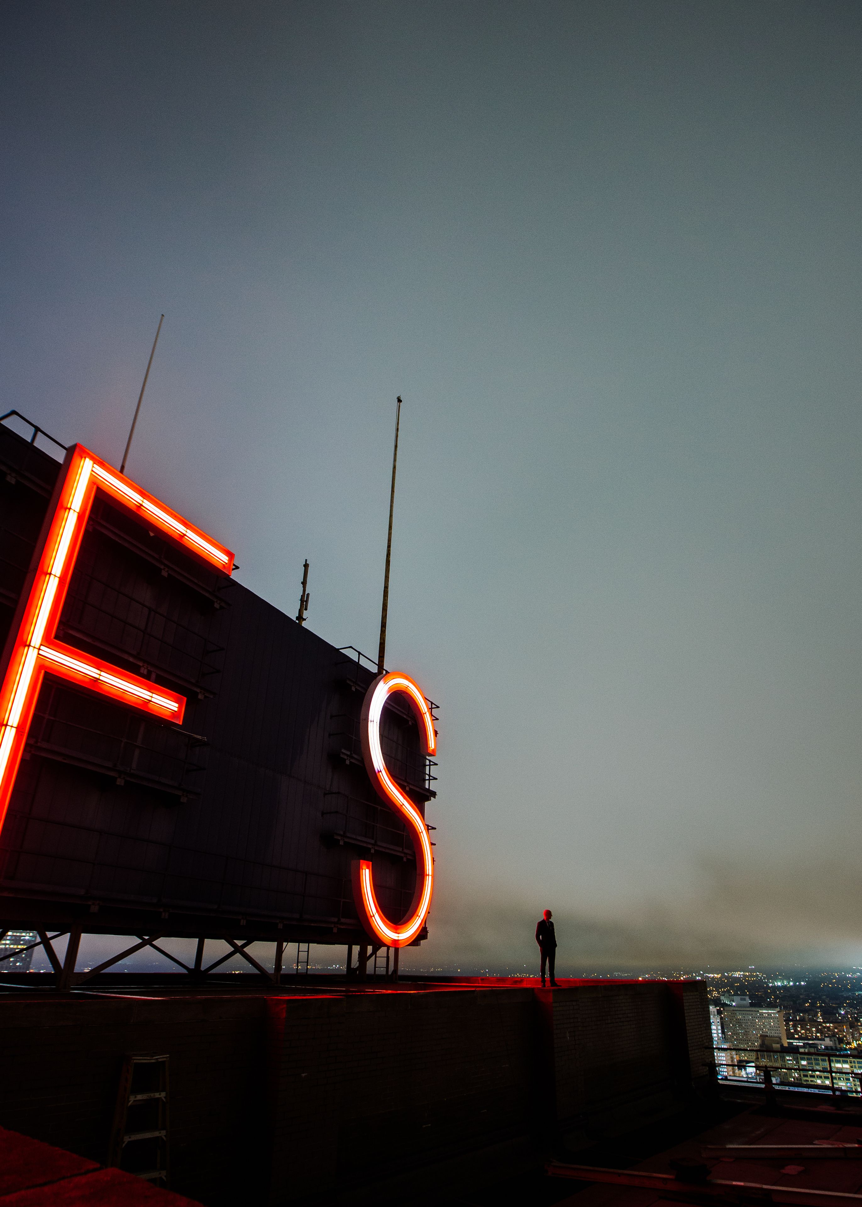 Une grande enseigne lumineuse en forme de « F » et de « S », fixée à la façade d’un immeuble, est visible la nuit et surplombe la ville.