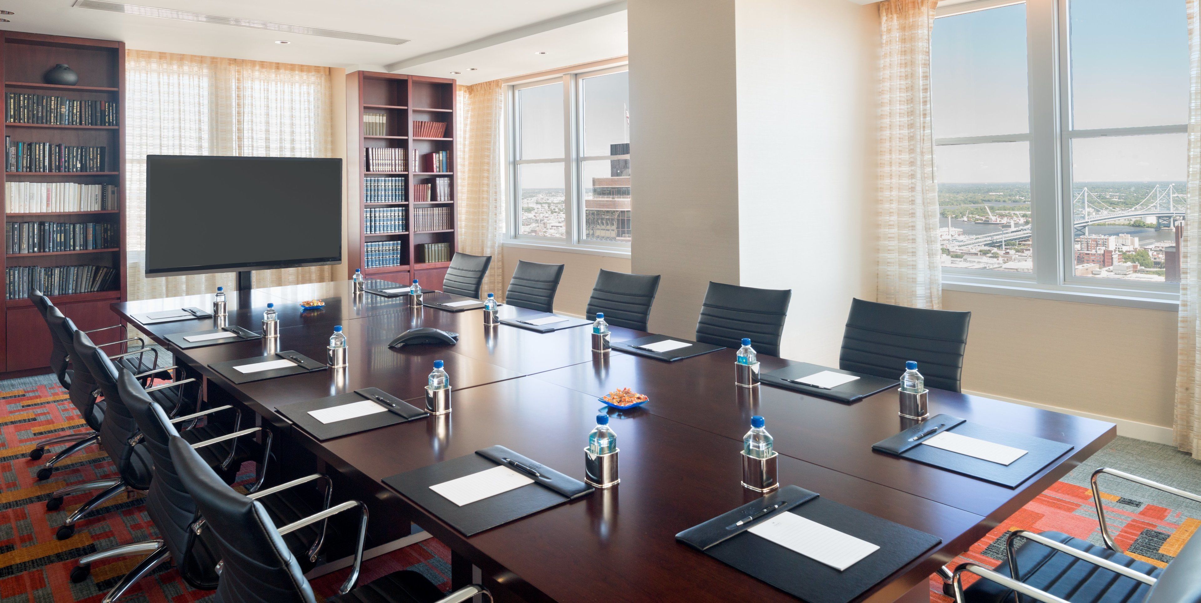 A conference room with a long table, chairs, a projector screen, and a bookshelf.