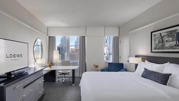 A hotel room with a bed, a desk, a chair, a television, and a view of the cityscape.
