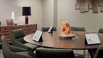 Un salón de conferencias con una mesa redonda, sillas tapizadas en verde, una tableta sobre la mesa y un elemento decorativo en la pared.