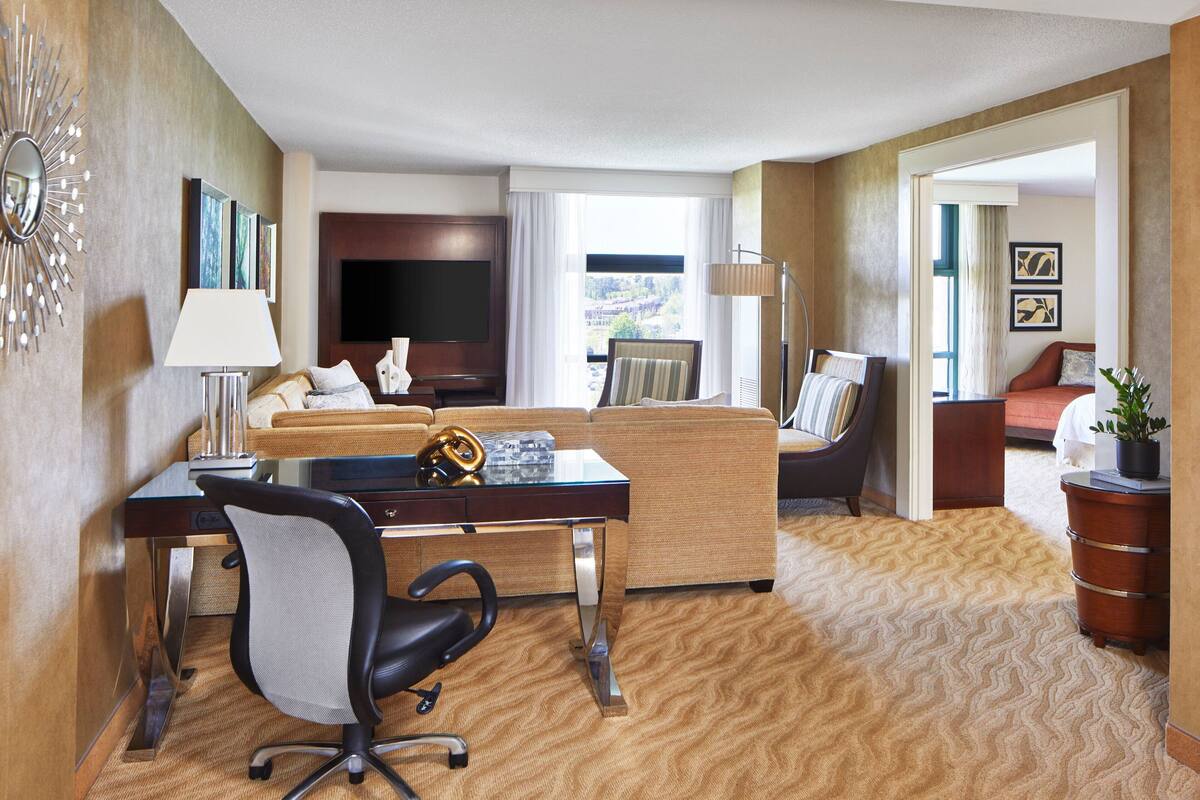 Habitación de hotel con sofá, escritorio con silla, televisor y vista al exterior.