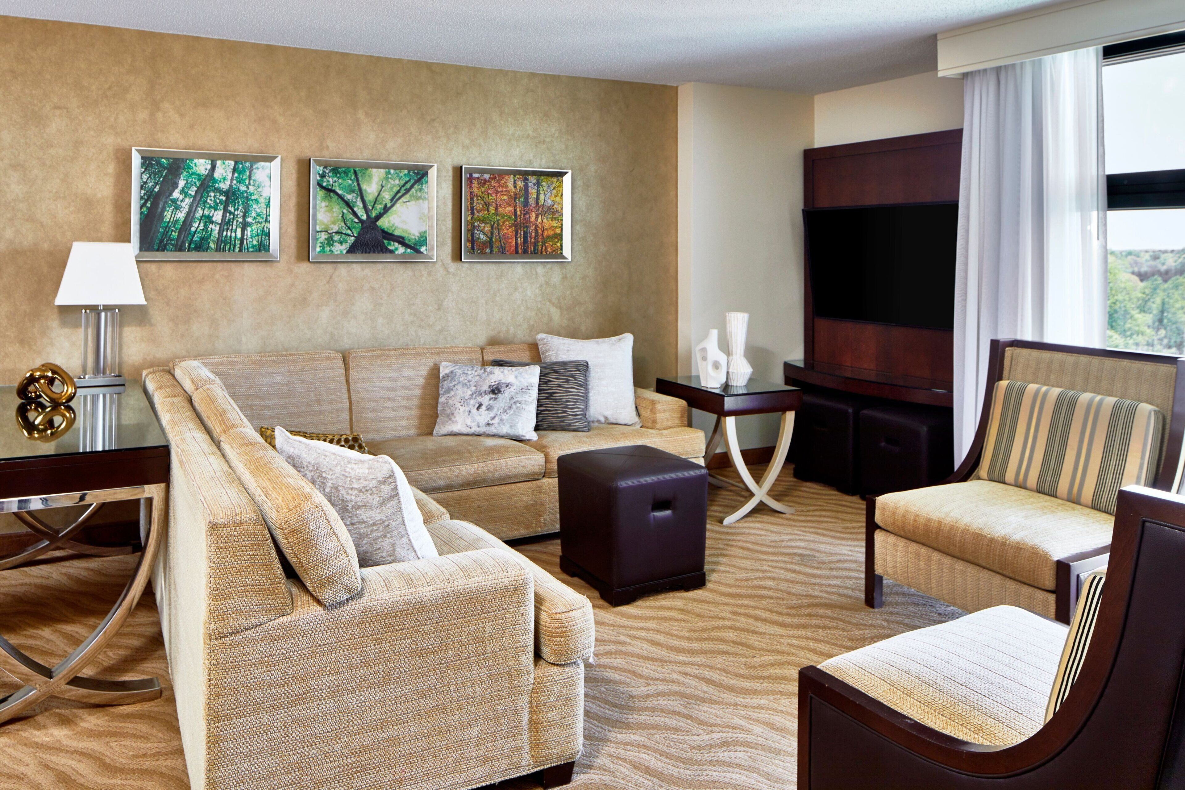 A hotel room with a beige sofa, a striped armchair, a small table with decorative items, and framed artwork on the wall.