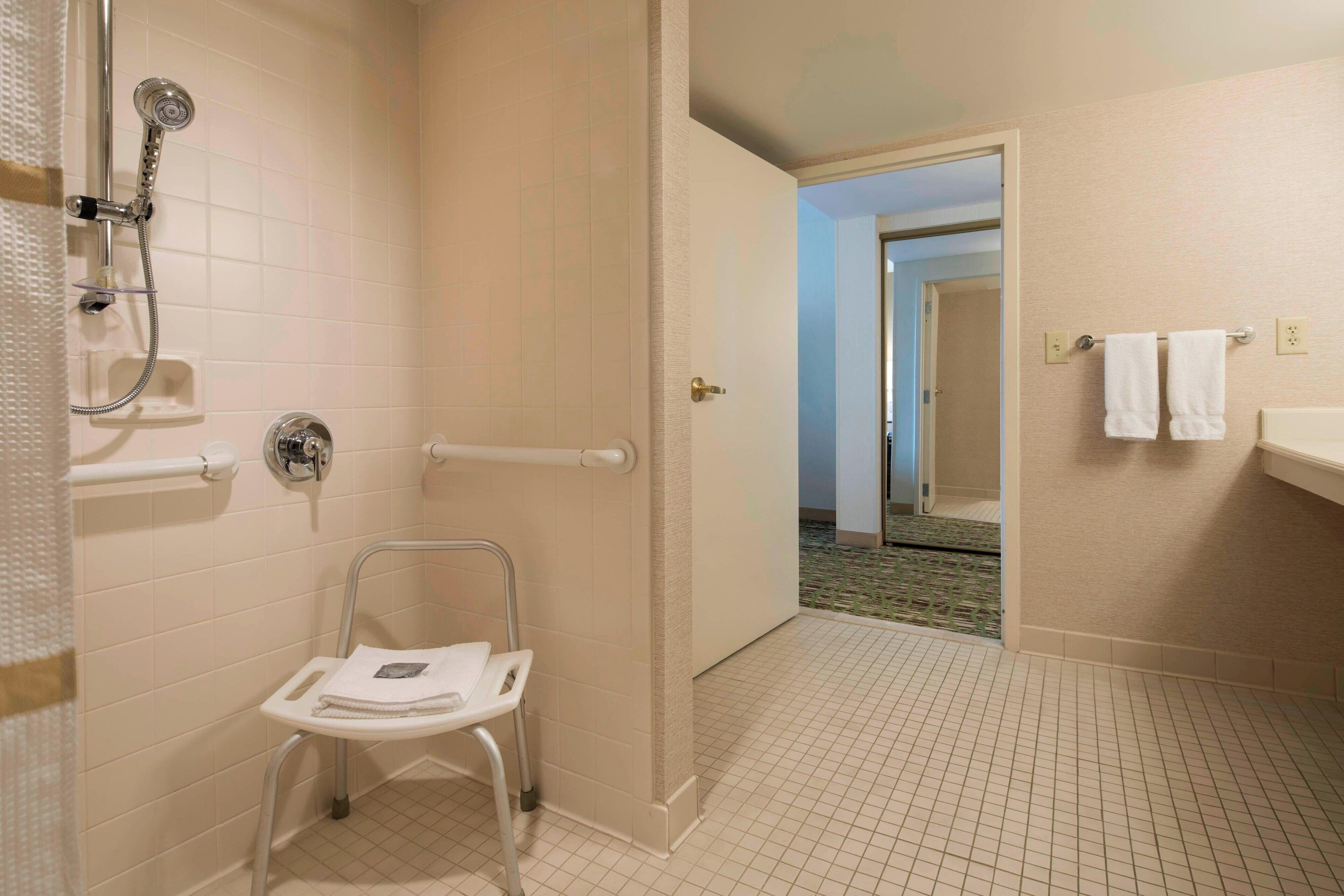 Un baño con ducha, barra de apoyo, barra de seguridad y banco accesible en silla de ruedas.