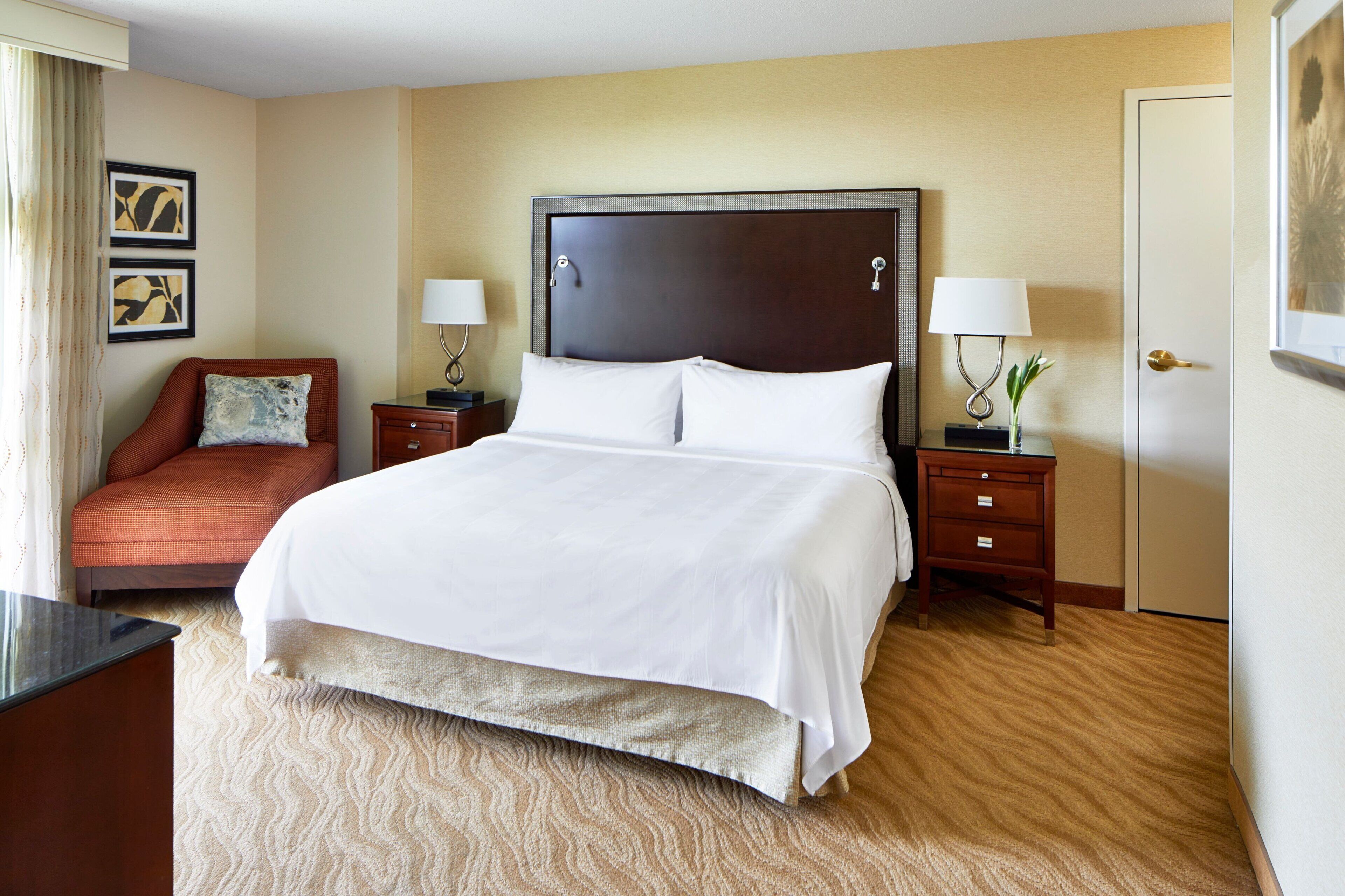 A hotel room with a large bed, two nightstands, a desk, a chair, and a door.