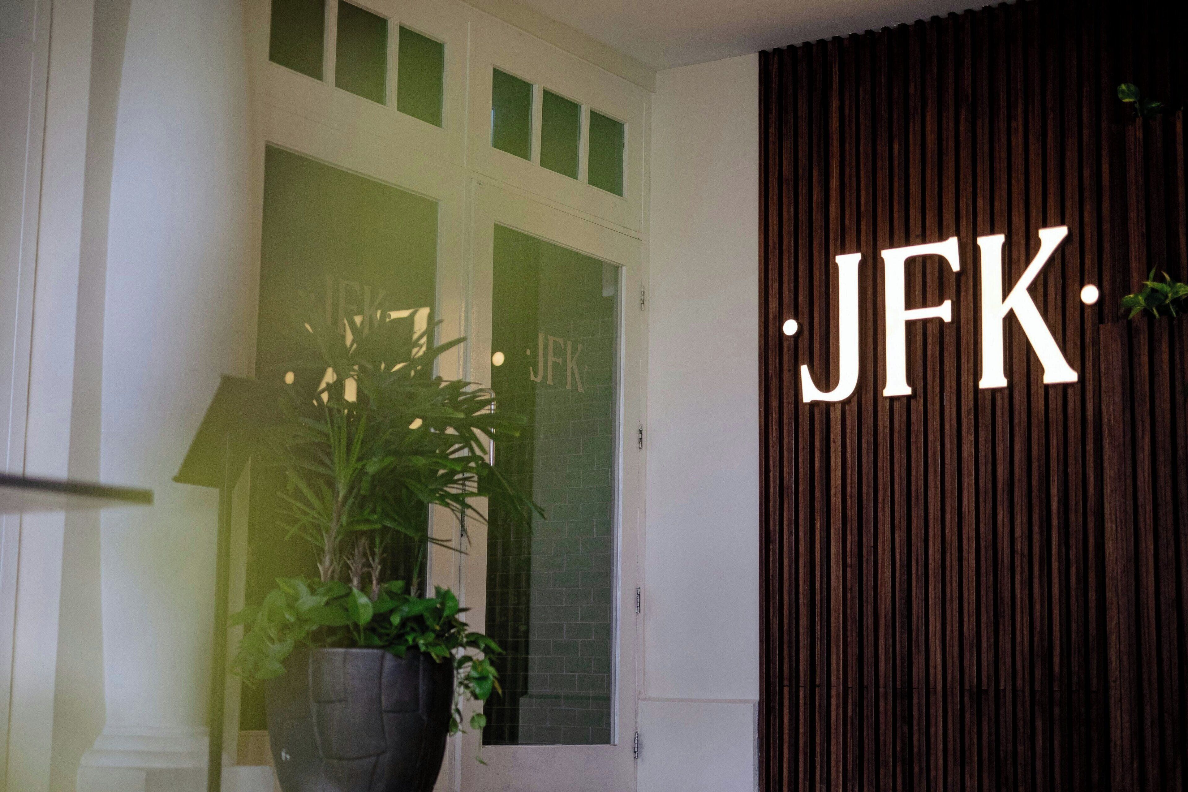 A door with a sign reading "JFK" and a large potted plant beside it.