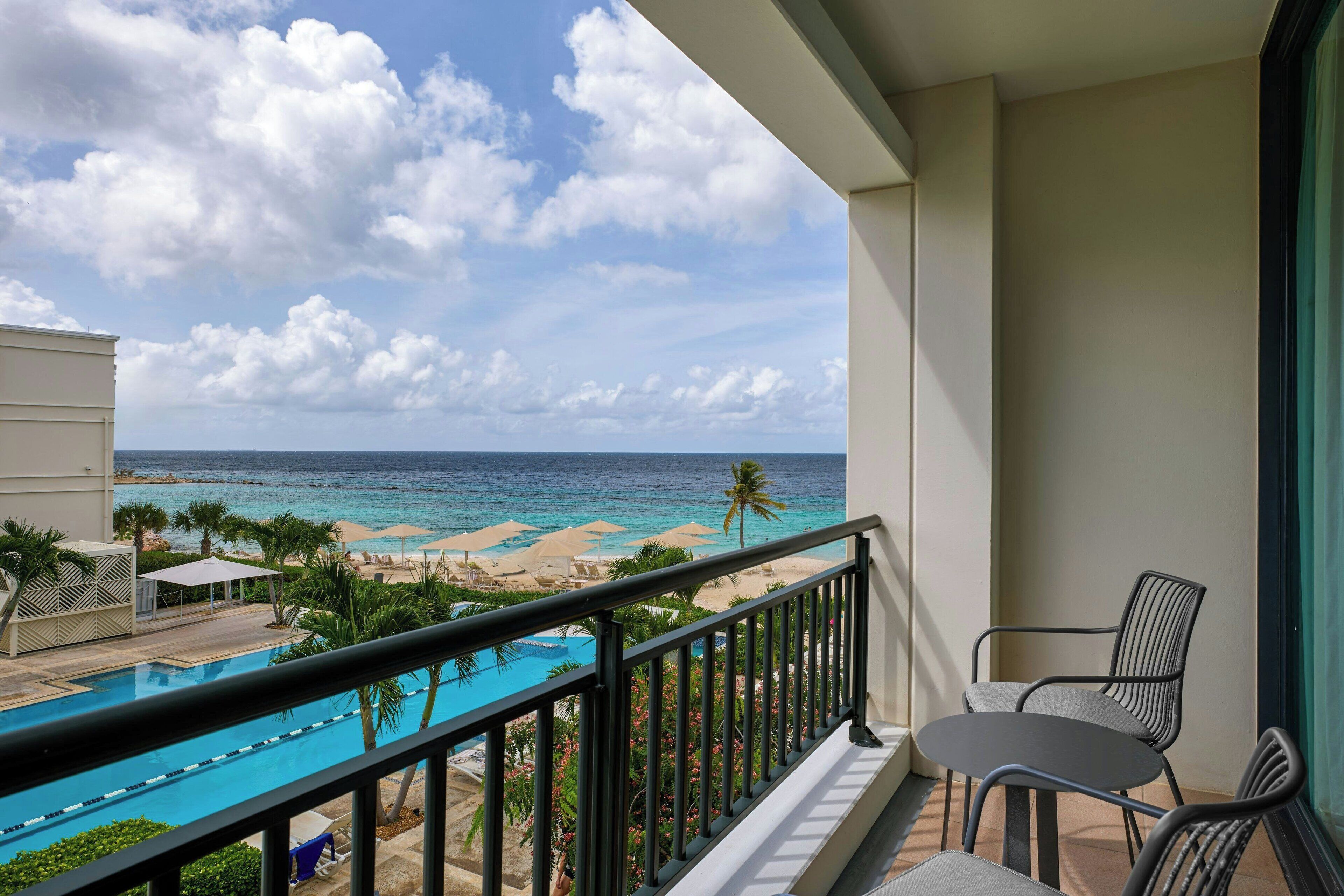 Ein Balkon mit Pool, Strandblick und Sitzgelegenheit im Freien.