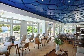 A spacious indoor area with a modern ceiling design, large windows offering views of the outdoors, and a variety of seating arrangements.