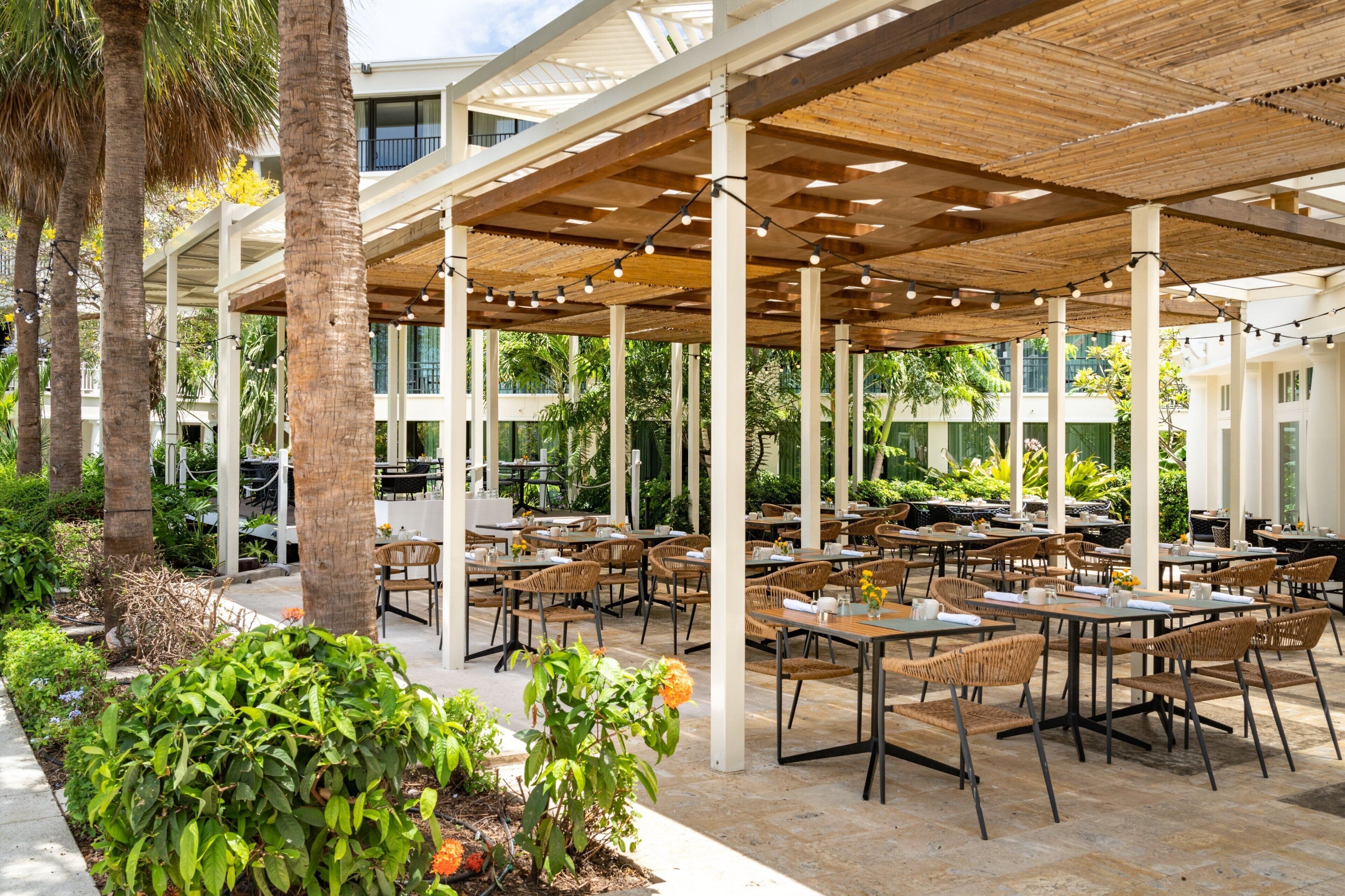 An outdoor patio area with tables and chairs, surrounded by palm trees and plants.