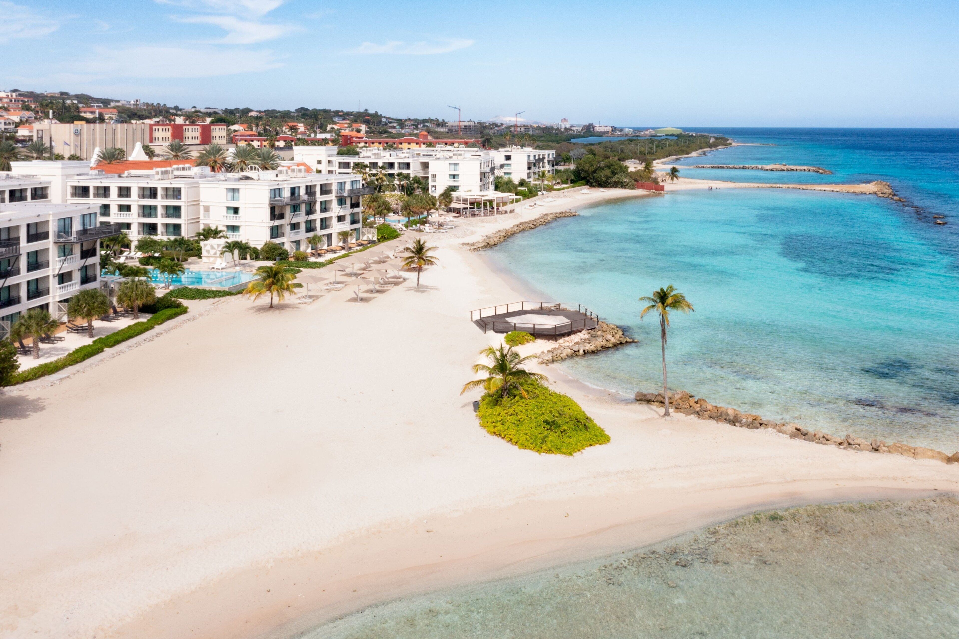 A beachfront hotel with multiple buildings, a sandy beach, and clear blue waters.
