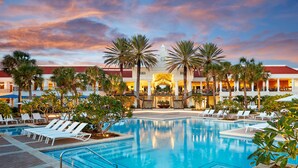 Ein Hotel mit Swimmingpool, Palmen und einem Gebäude mit rotem Dach.