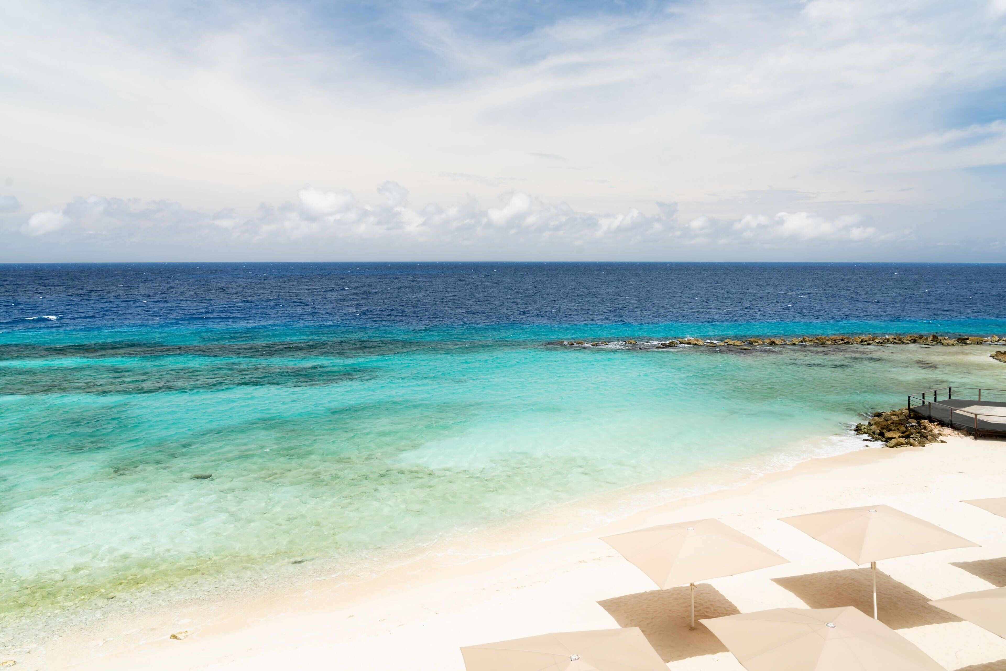 Uma praia com águas azul-turquesa cristalinas, areal arenoso e guarda-sóis.