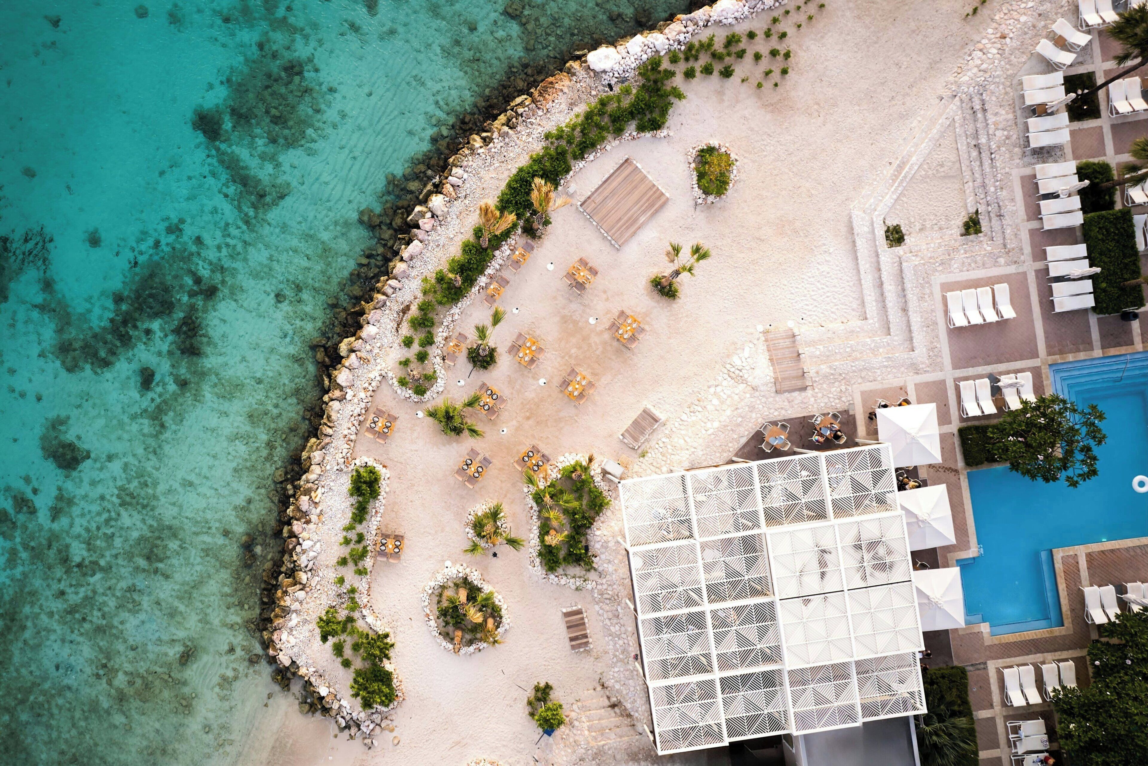 An aerial view of a beach resort with a pool, sun loungers, and a covered seating area.