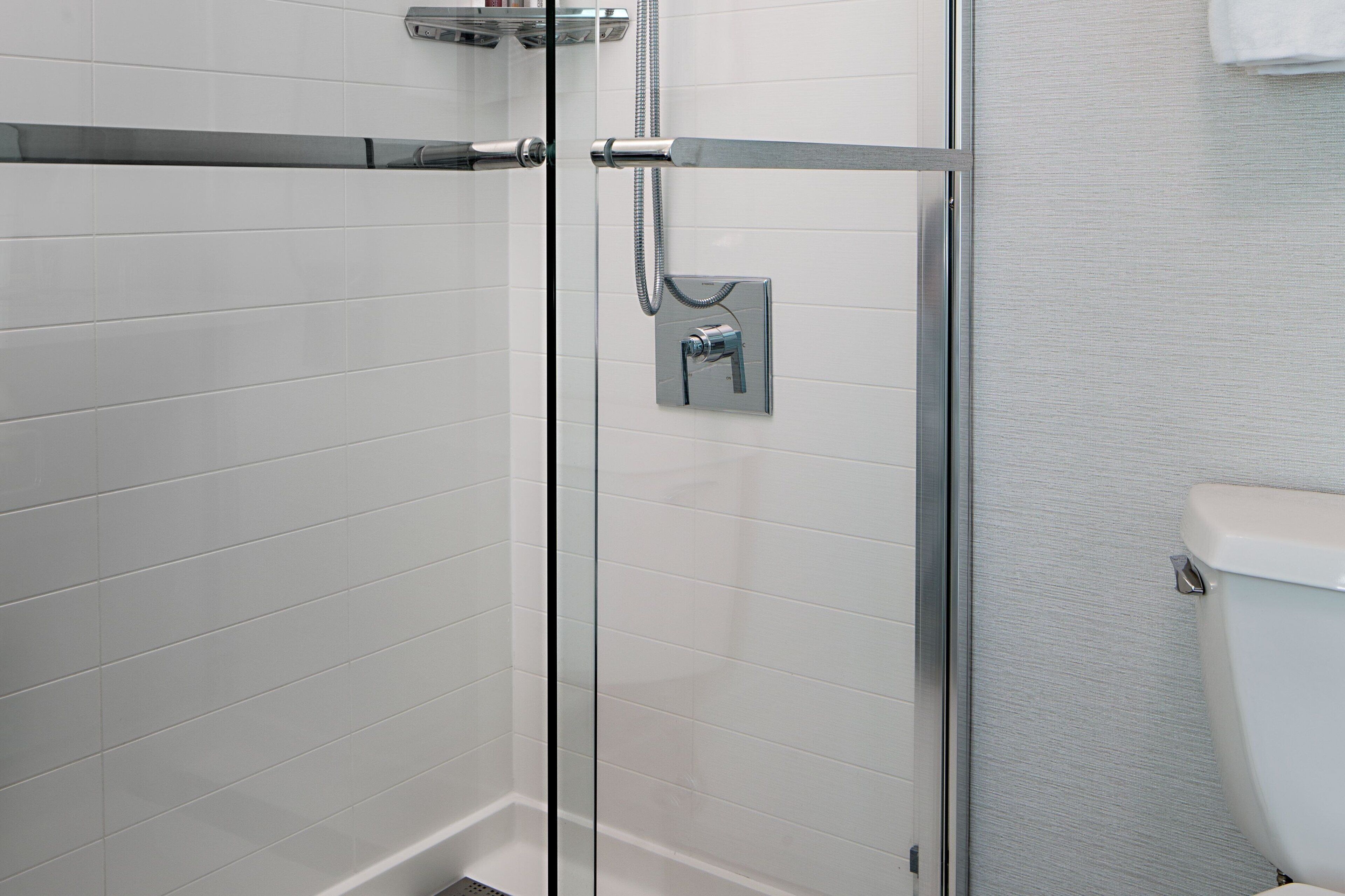 A glass-enclosed shower with a chrome faucet and hose, adjacent to a white tiled wall and a toilet.