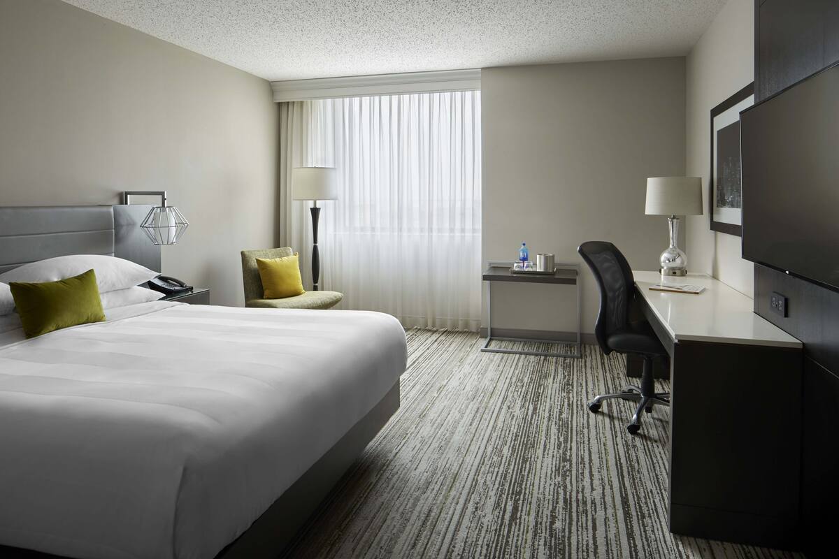 A hotel room with a large bed, a desk, a chair, a television, and a window with curtains.