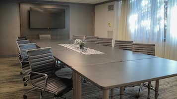 A conference room with a long table, six chairs, a projector screen, and a large window with curtains.