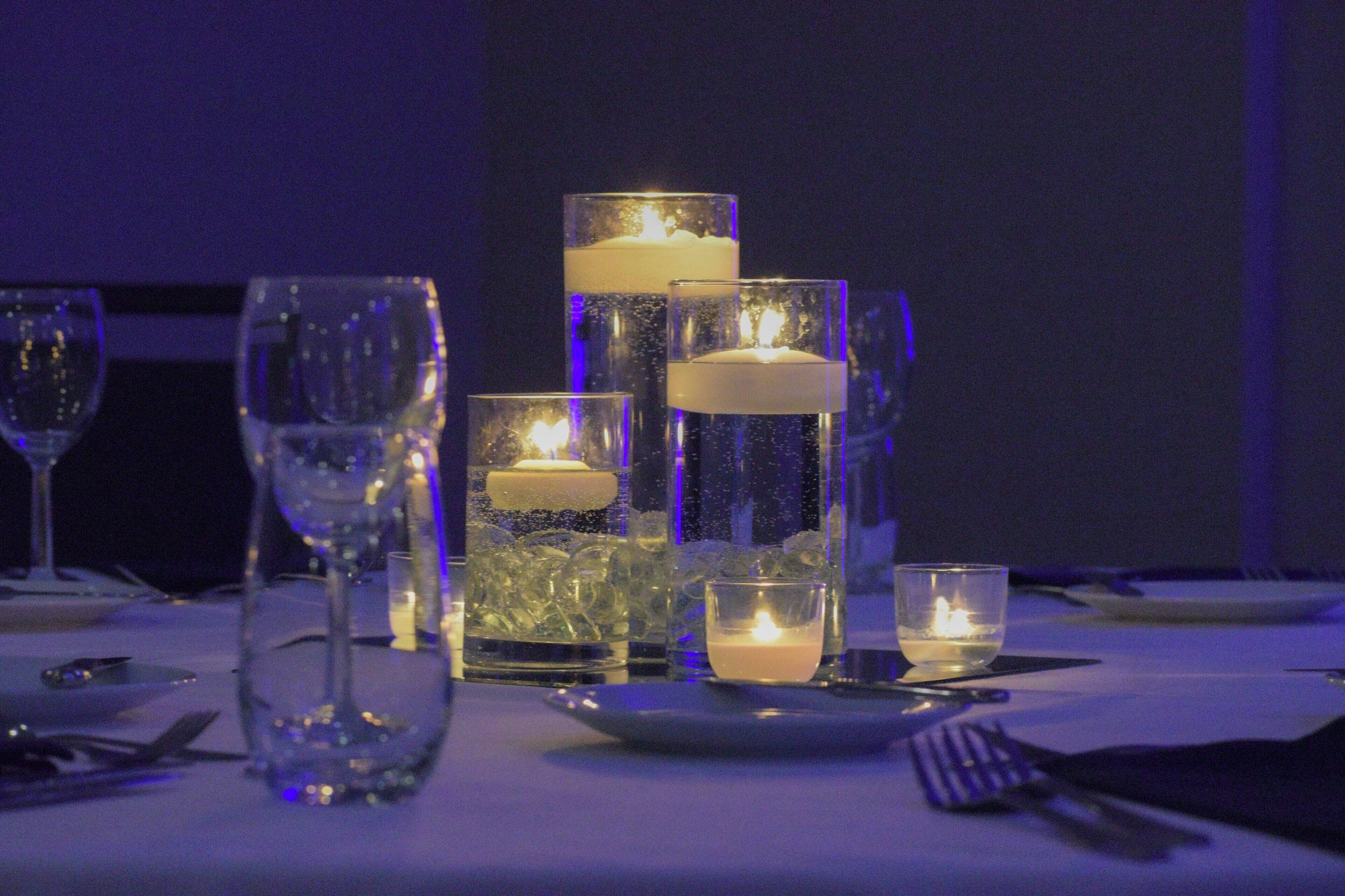 Una mesa dispuesta para comer con varios vasos, una vela y un vaso de agua.
