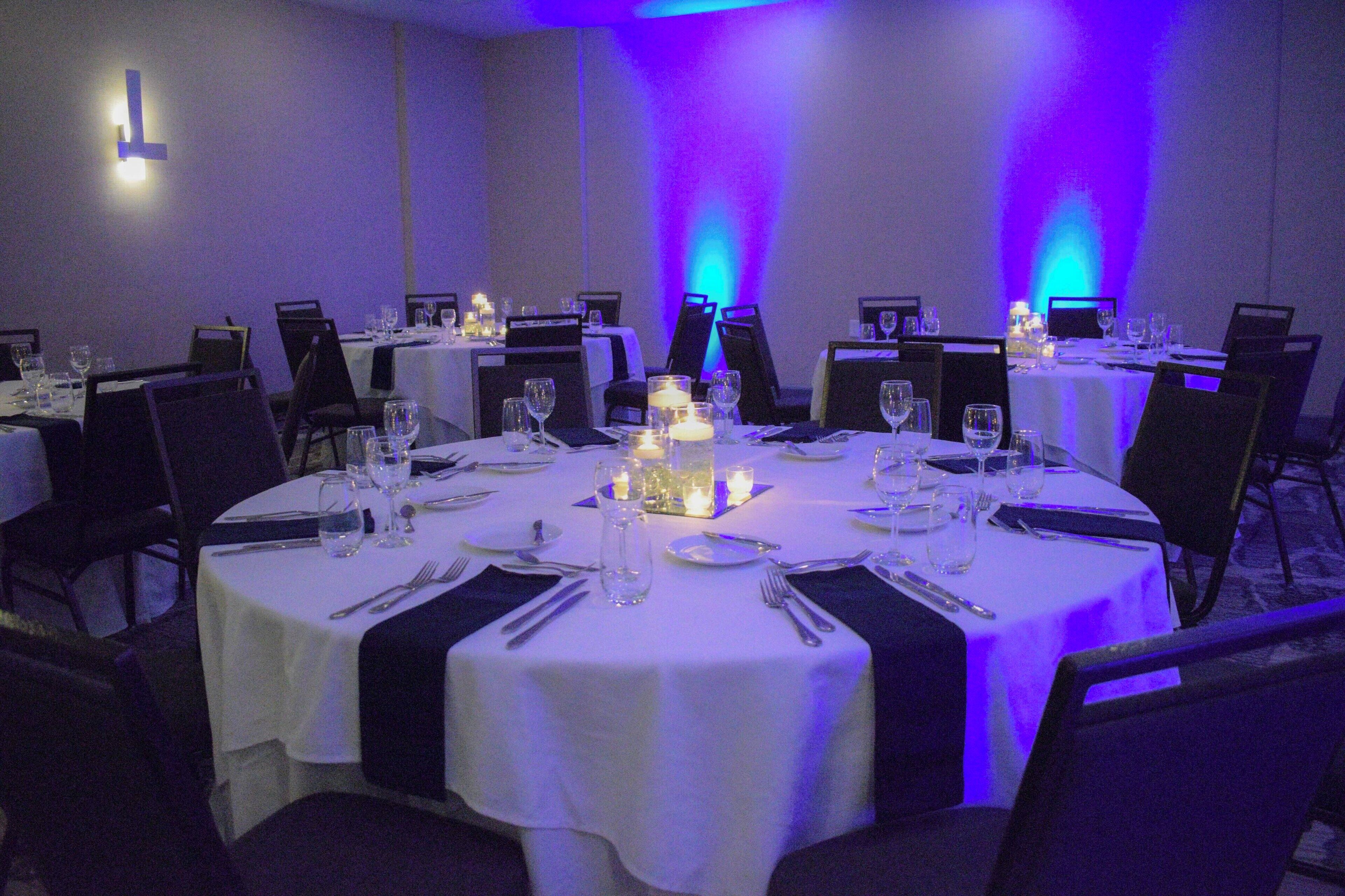 A conference room with round tables, chairs, and a white tablecloth.
