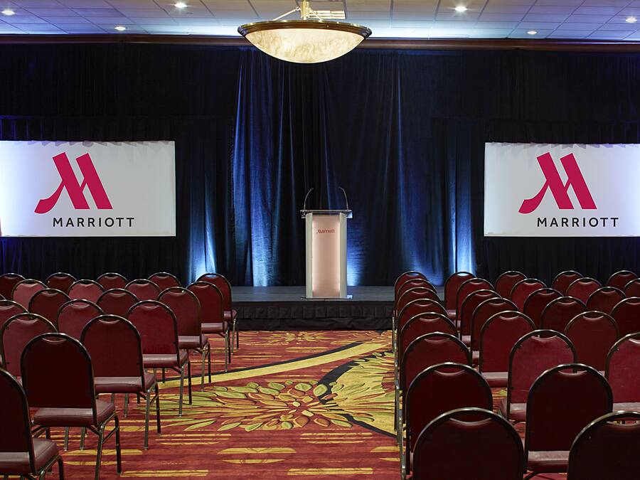 A conference room with rows of red chairs, a podium, and two screens displaying the Marriott logo.