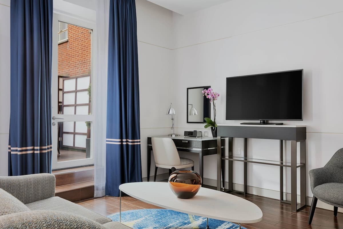 A modern hotel room with a flat-screen TV, a desk with a computer, a comfortable sofa, and a large window with curtains.