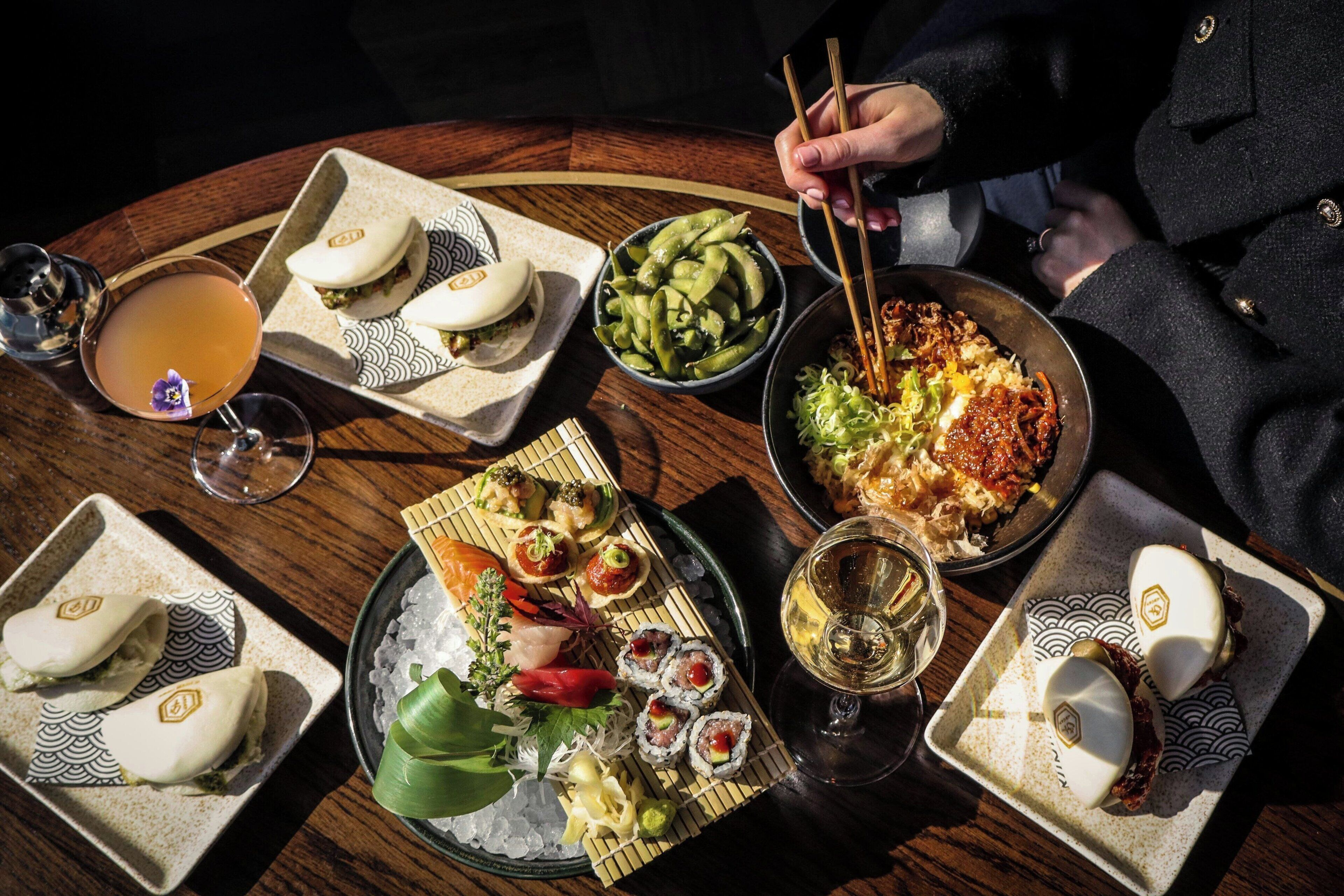 A table with various Japanese dishes, including sushi and edamame, and a glass of sake.