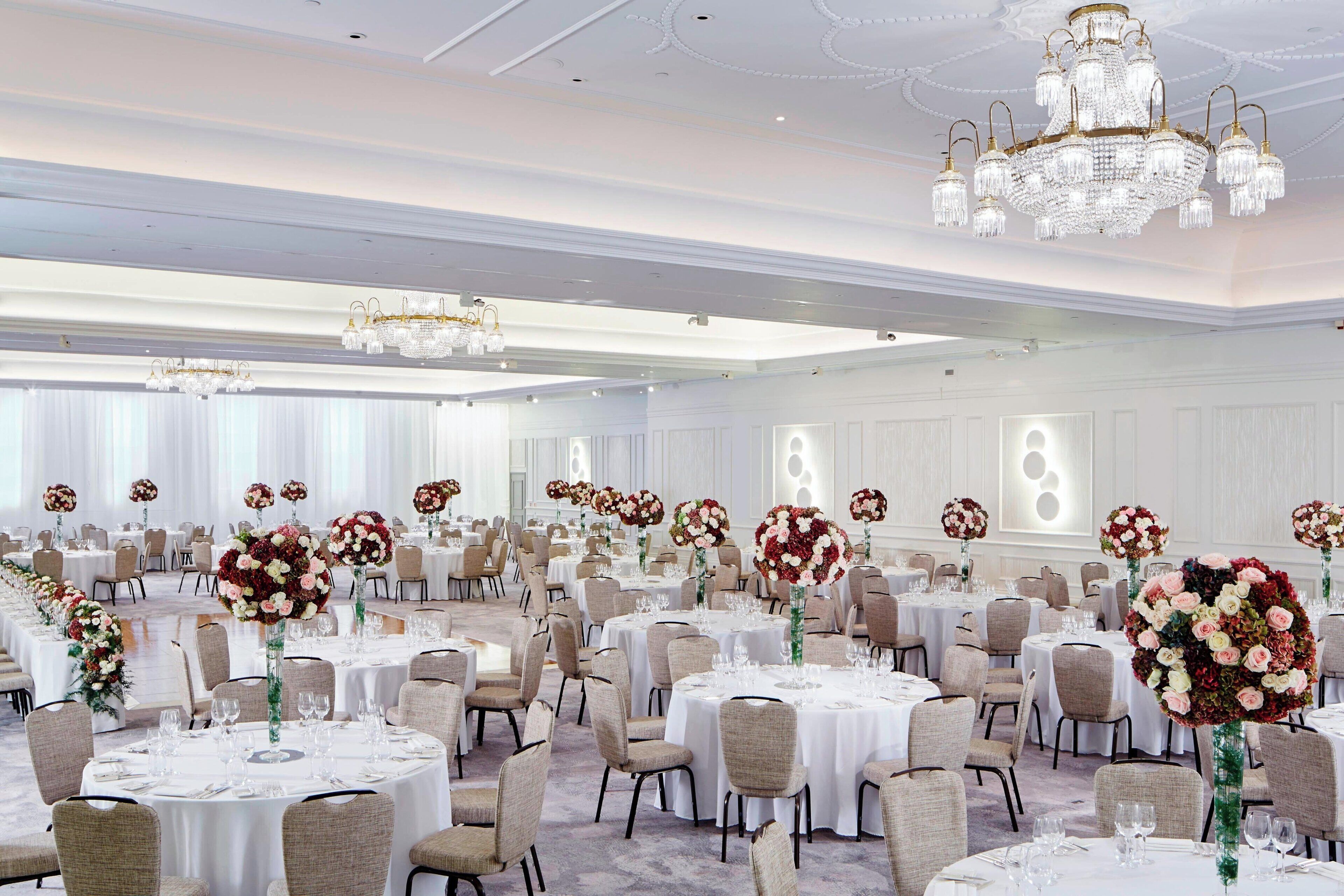 A banquet hall with round tables, chairs, and floral centerpieces.