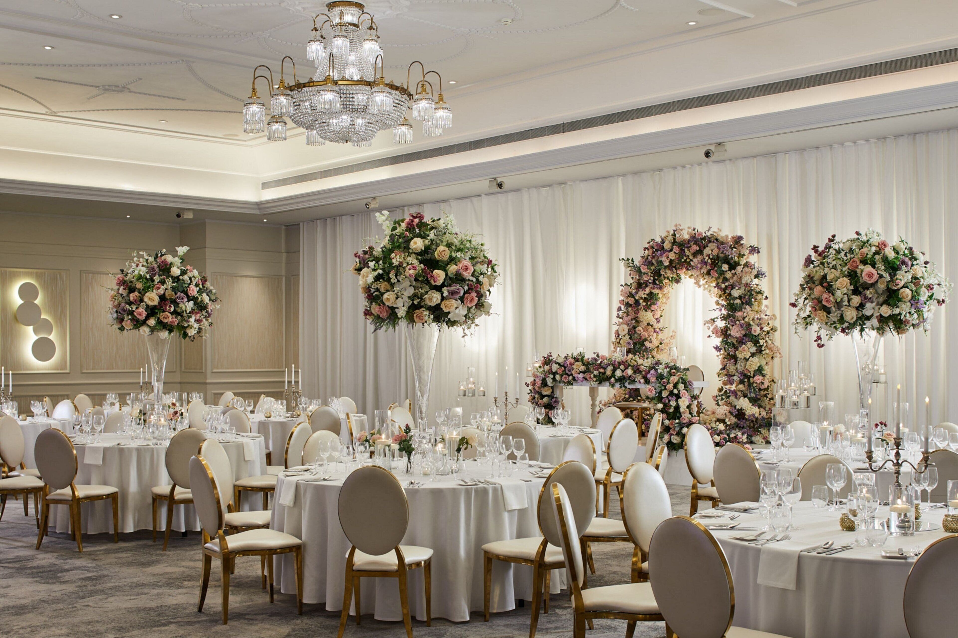 A banquet hall with round tables, white tablecloths, and gold chairs.