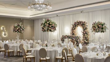 A banquet hall with round tables, white tablecloths, and gold chairs.