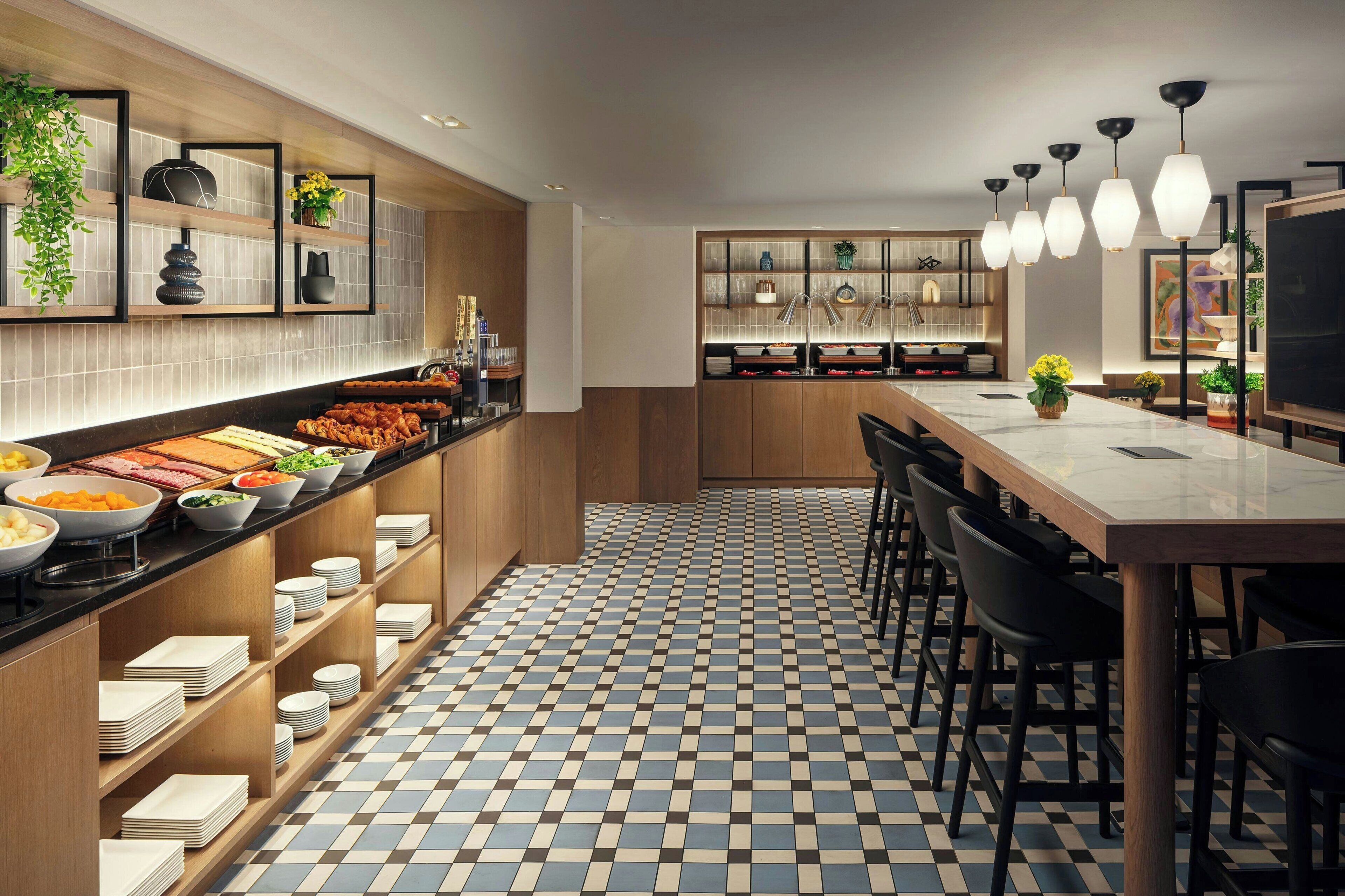 A modern kitchen with a checkered floor, wooden shelves, and a long counter with food items.