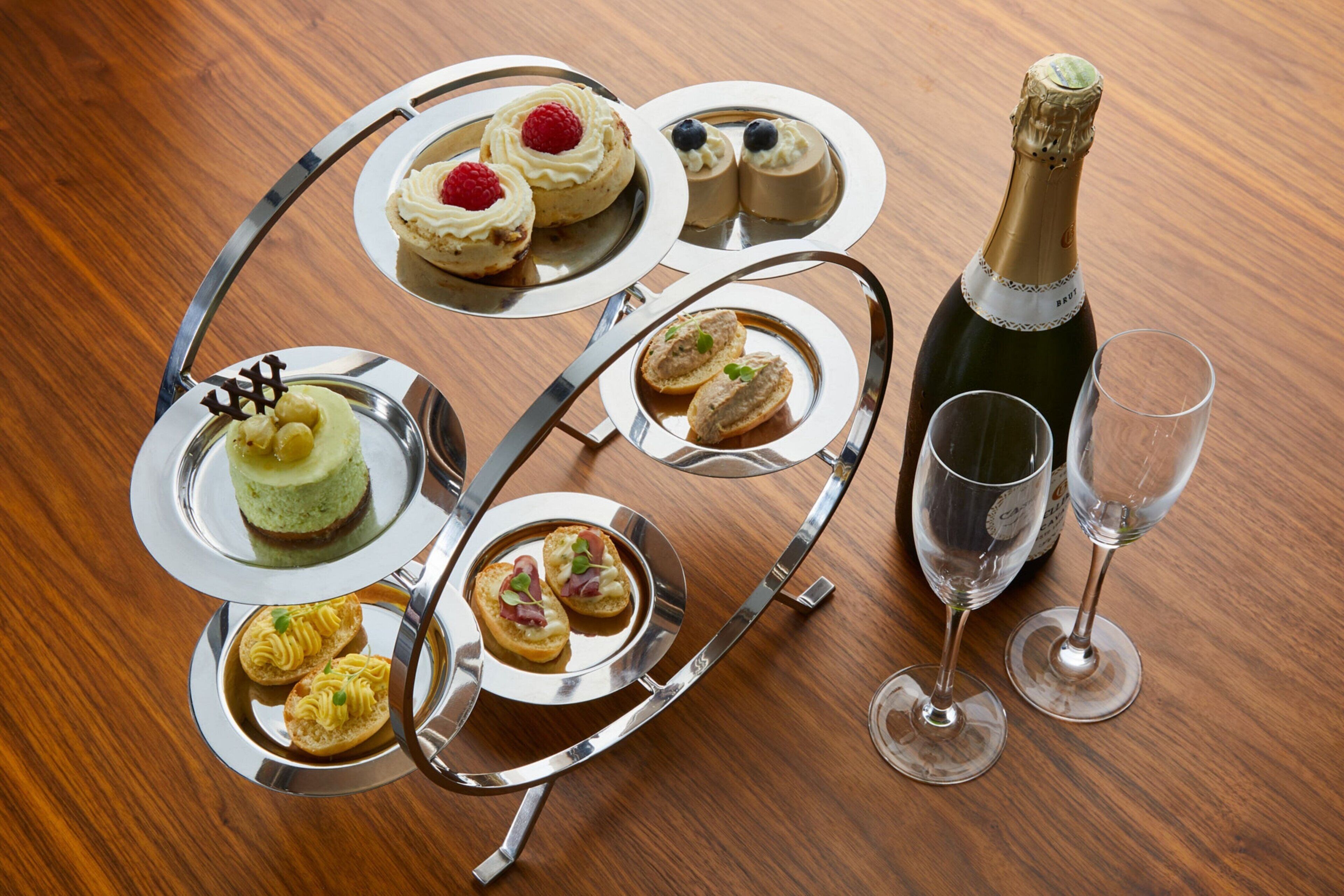 A multi-tiered dessert tray with various pastries and a bottle of champagne on a wooden table.
