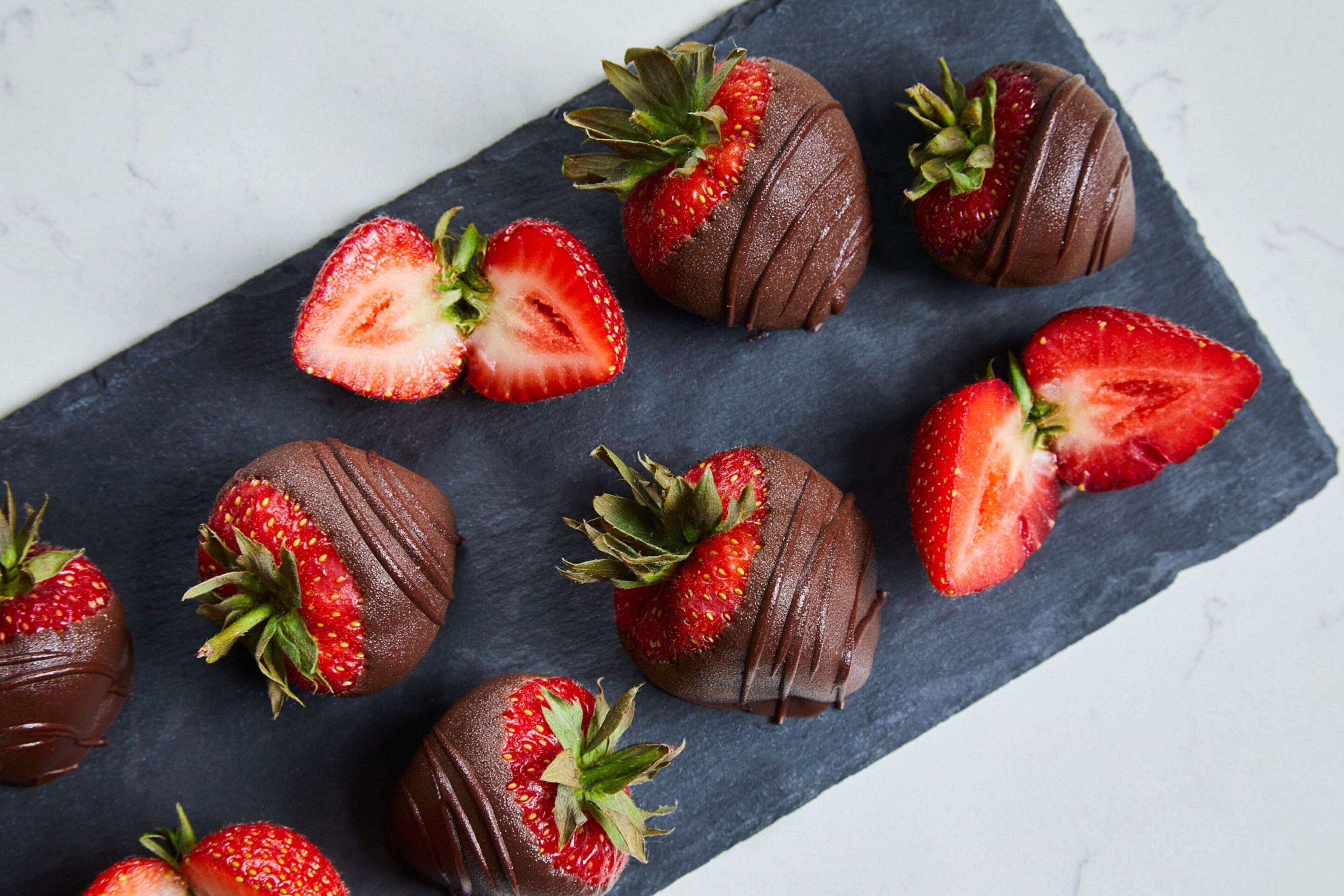 A slate board with chocolate-covered strawberries, some cut in half.