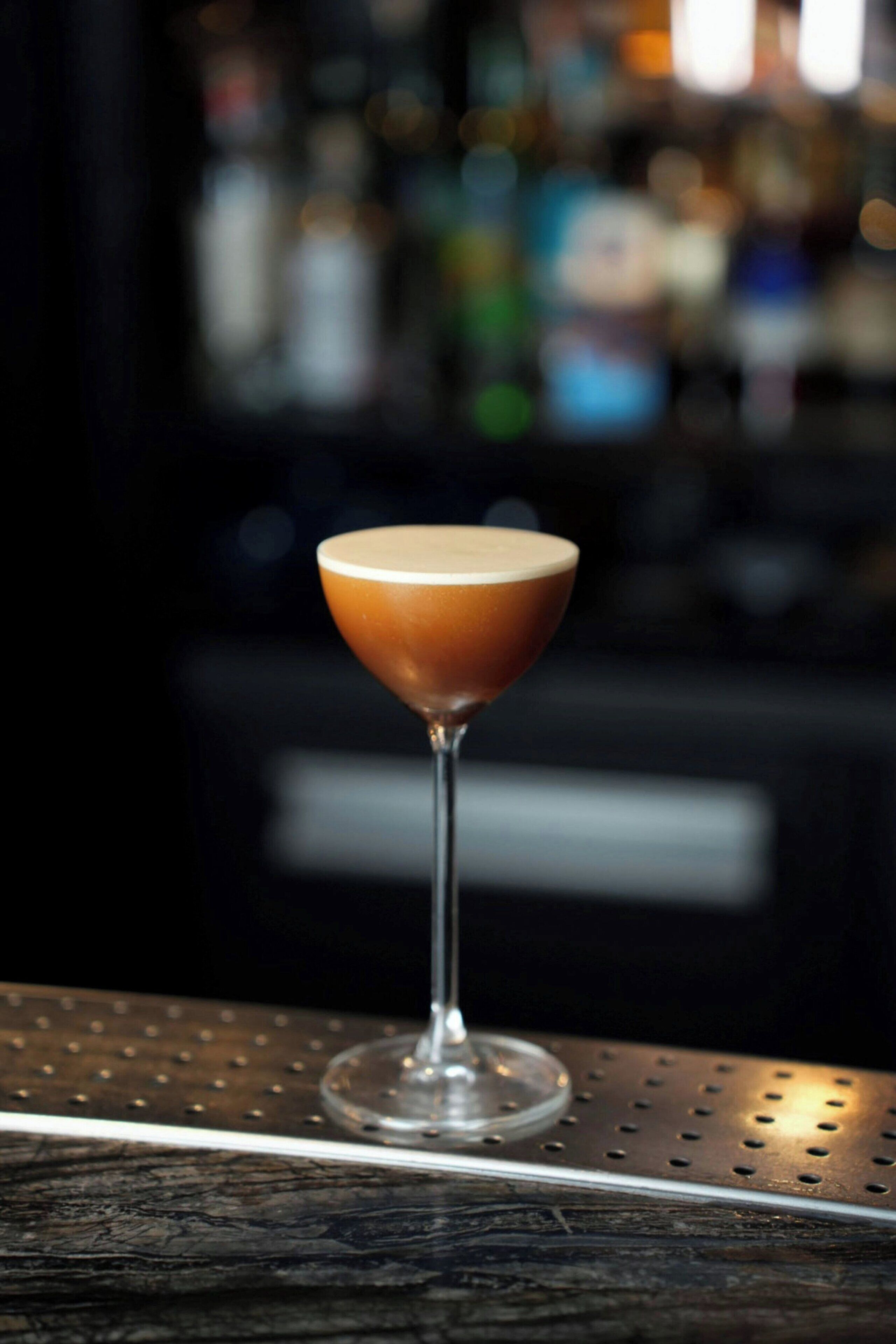 A martini glass with a frothy top on a metal bar counter.