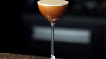 A martini glass with a frothy top on a metal bar counter.