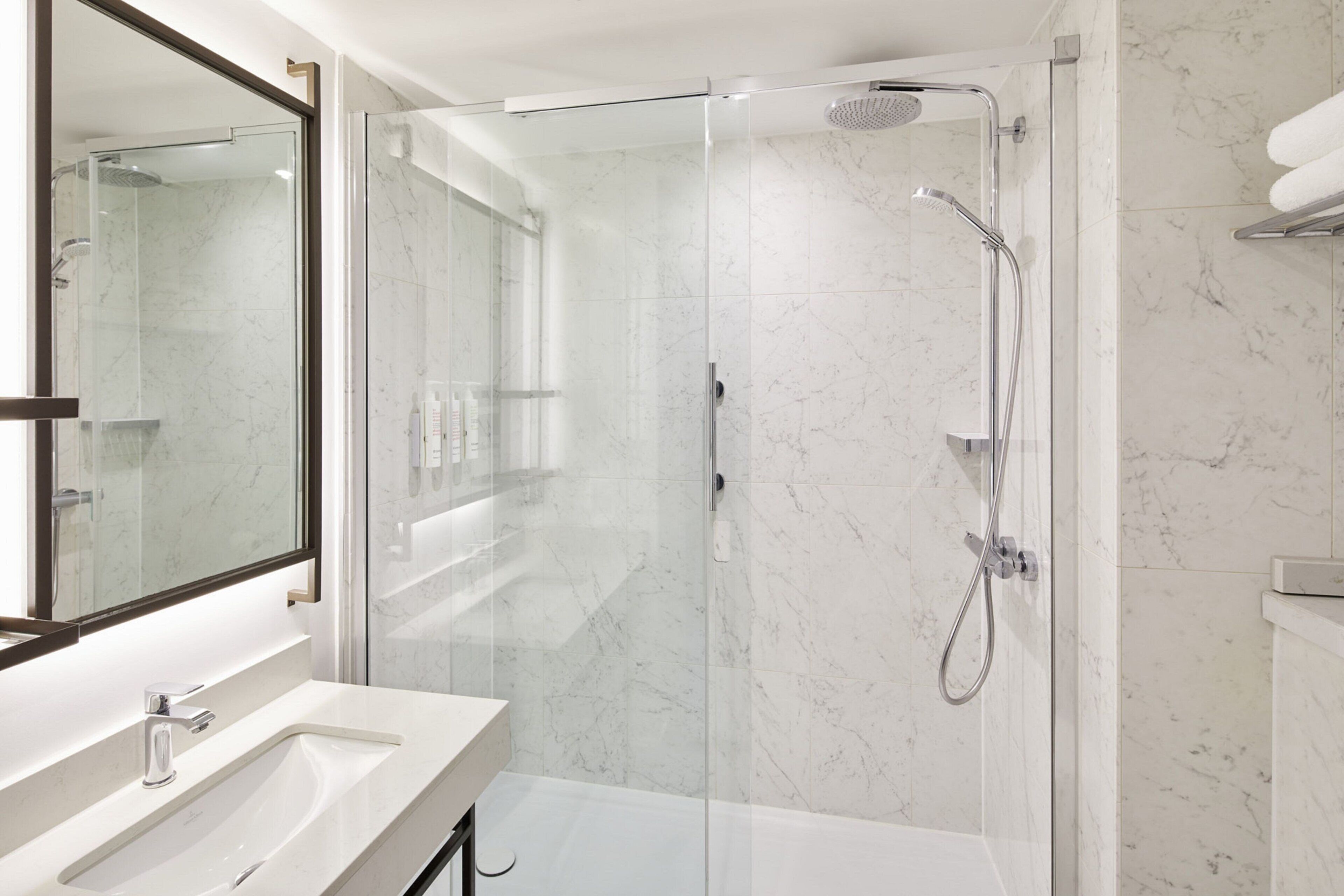 A modern bathroom with a glass-enclosed shower, a white sink, and a large mirror.