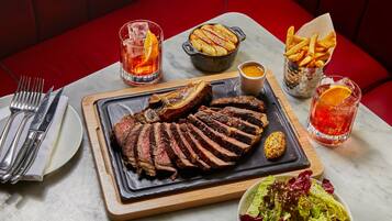 Una mesa de comedor con un bistec, papas fritas y ensalada, acompañada de bebidas y cubiertos.