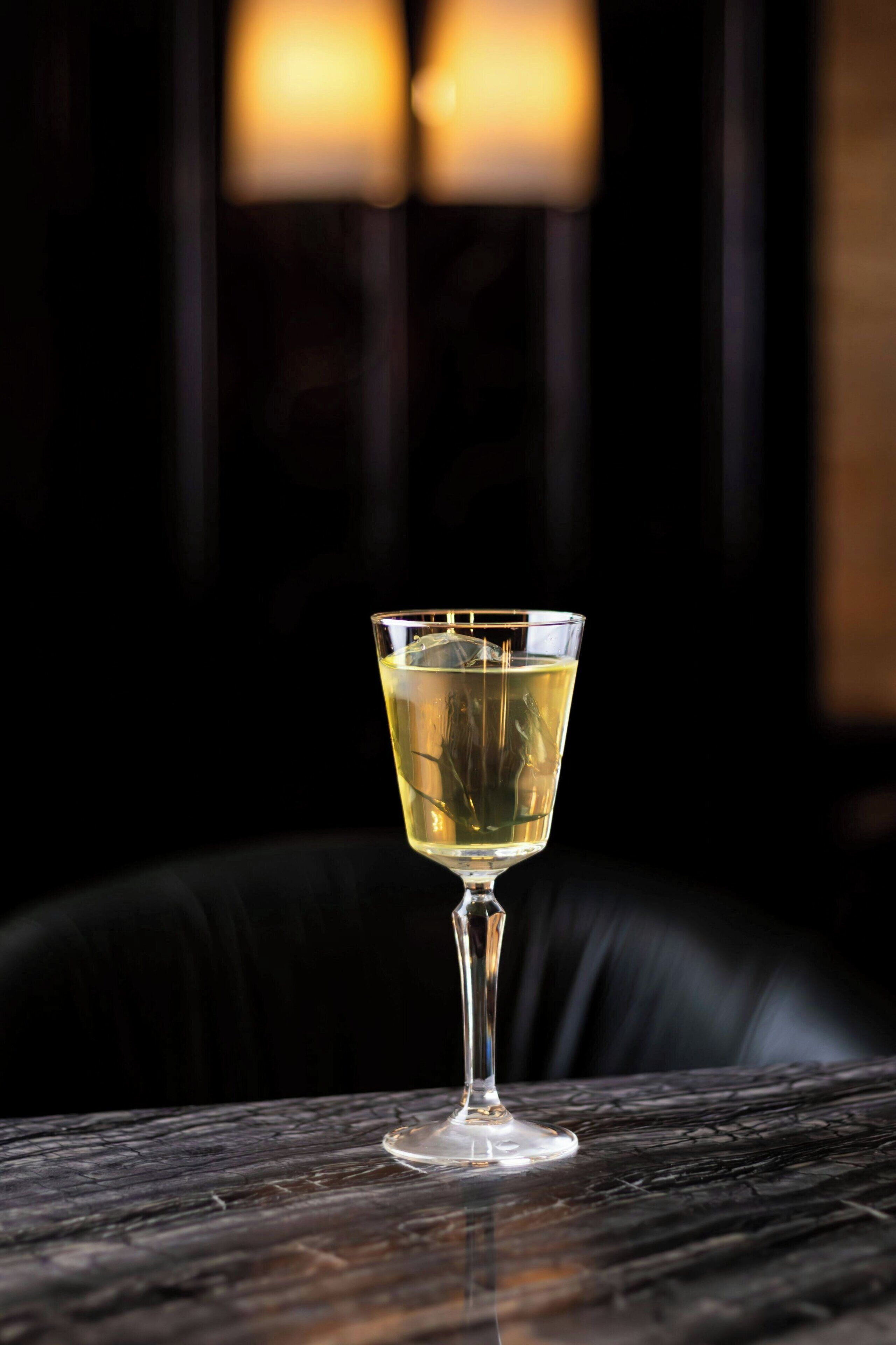 A clear glass of a light-colored beverage on a wooden table with a dark background.